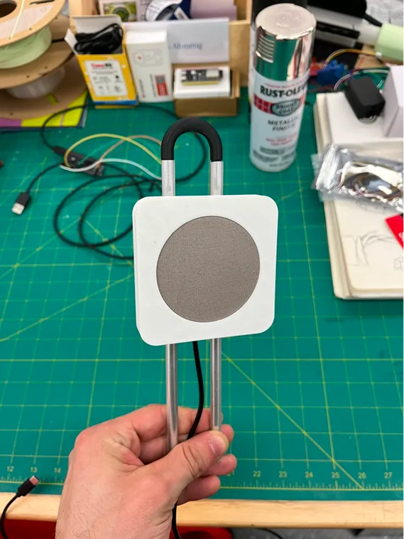 A hand holding a white prototype sensor head on aluminum rods at a workbench
