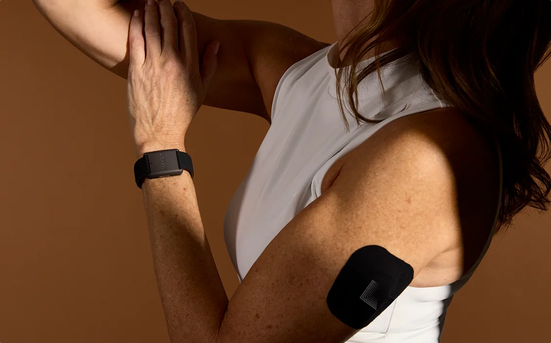 A woman wearing the Limbo band and sensor on her arm, against a warm brown background