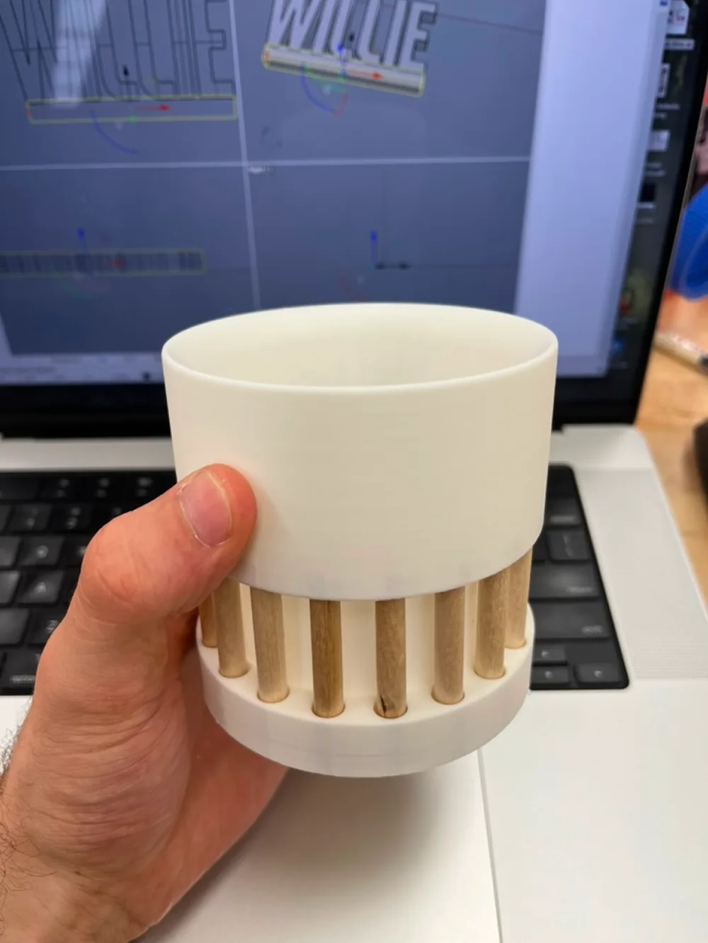 A hand holding a white printed mug with wooden dowels around its base
