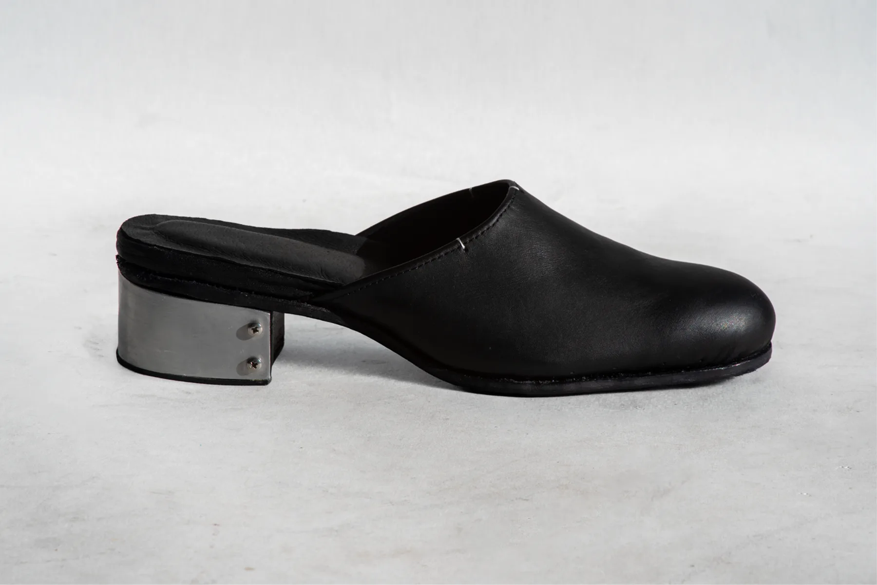 Black leather mule with a hand-rolled aluminum heel, side view
